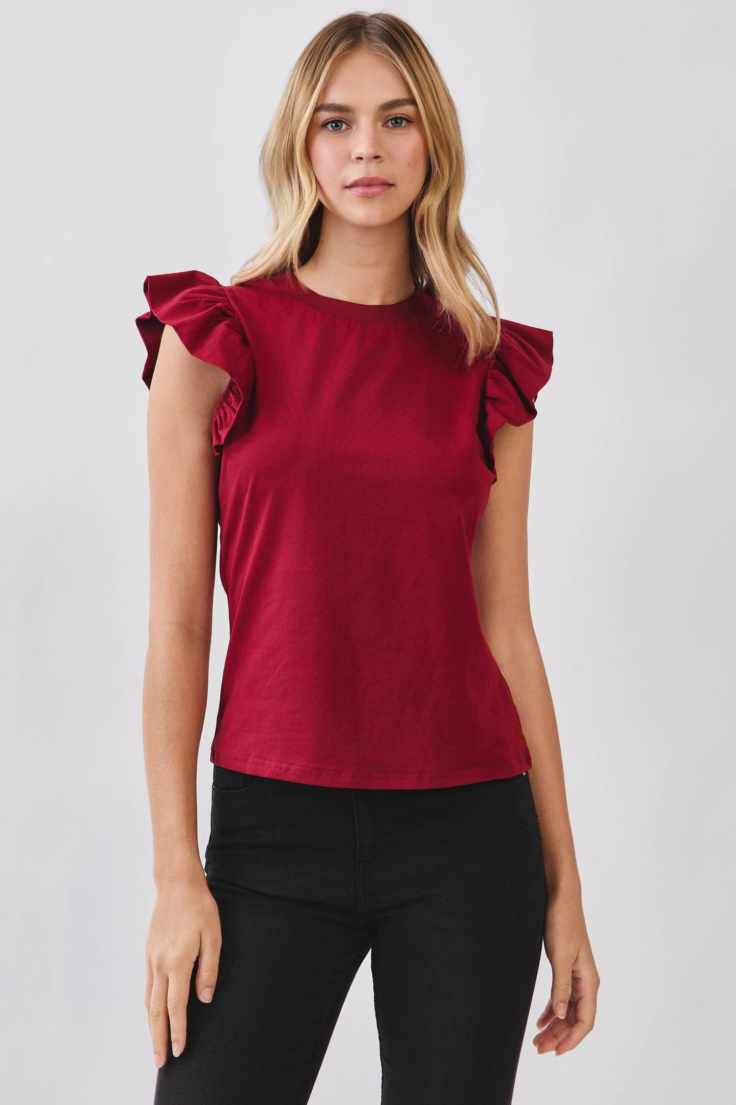 Woman wearing a red top with ruffled shoulders against a white background