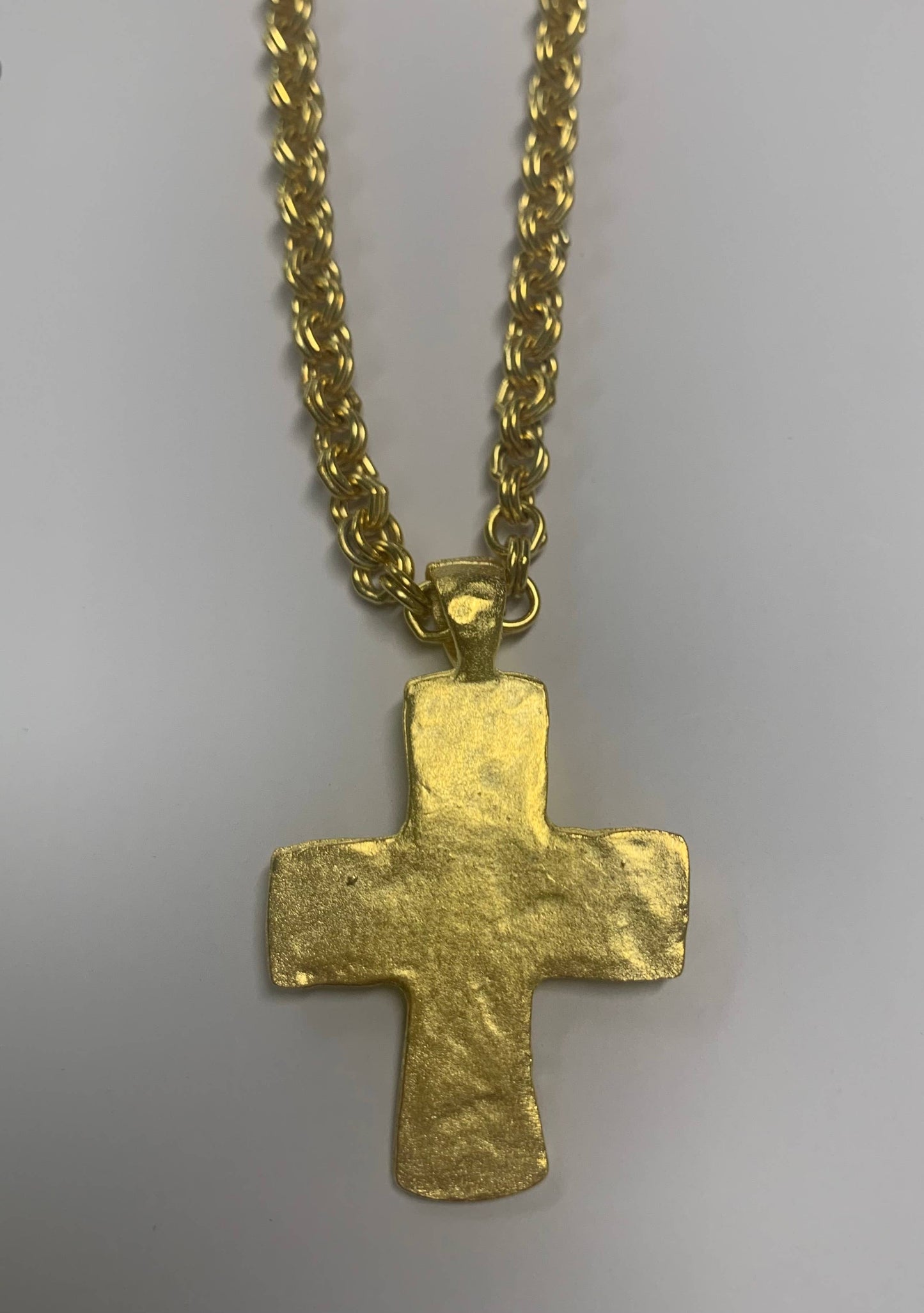 Gold cross pendant on a chain against a gray background