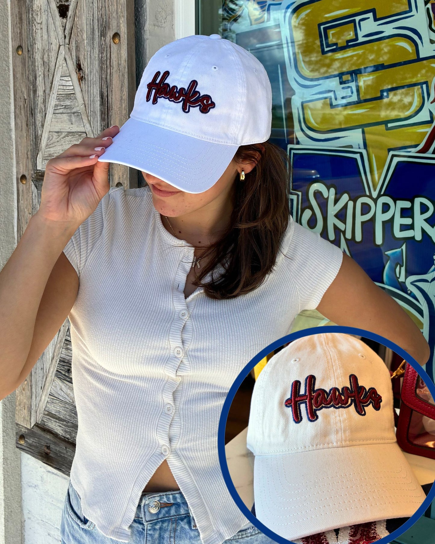 A woman wearing a white baseball cap with 'Hawks' embroidered in Navy and Crimson script, paired with a white ribbed short-sleeve top and denim jeans. A circular inset shows a close-up of the cap's front embroidery.