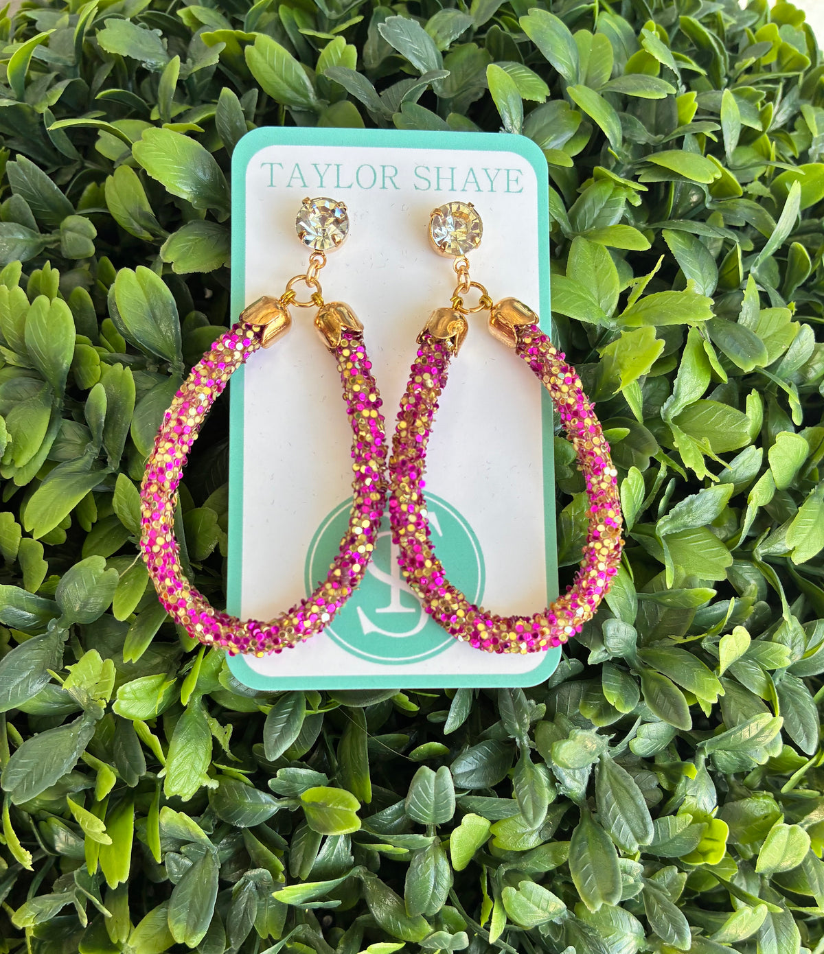 purple and gold teardrop hoops against a green leaf background