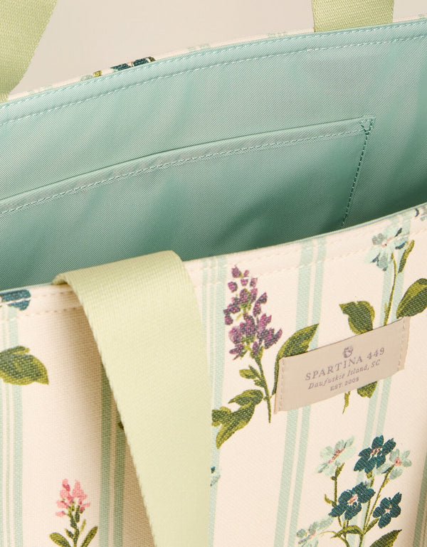 Close up of a tote bag featuring a floral pattern on a cream background, with light fabric shoulder straps, shown against a solid light beige background.