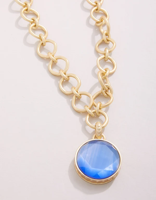 Gold chain necklace with a blue pendant on a light gray background