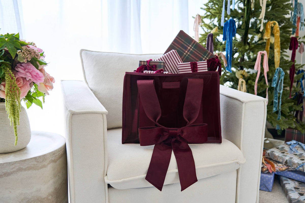 Red velvet bow tote bag on a white chair beside a Christmas tree