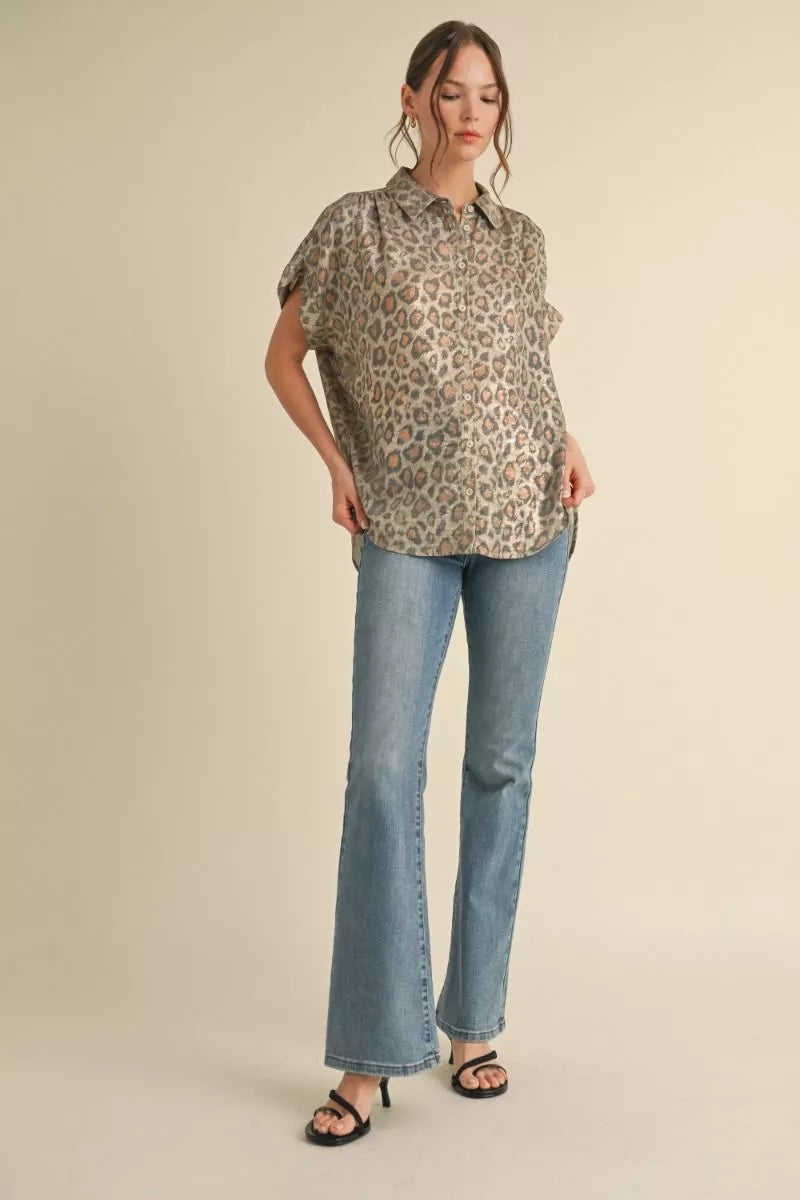 A woman modeling a short-sleeve leopard-print blouse with light-wash blue flare jeans and black slide sandals, standing against a plain beige studio background.