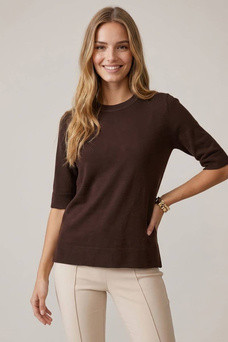 Woman wearing a brown sweater and beige pants against a plain background