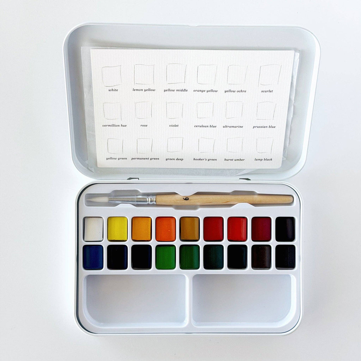 Open watercolor paint tin with 18 colors, mixing trays, and brush