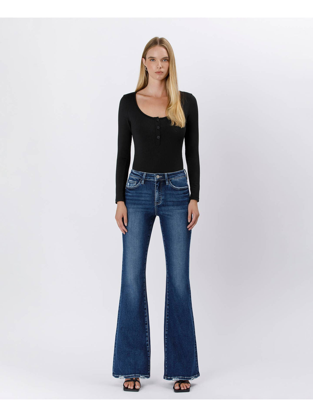 A woman modeling a black long-sleeve top and blue flare jeans against a plain light gray studio background.
