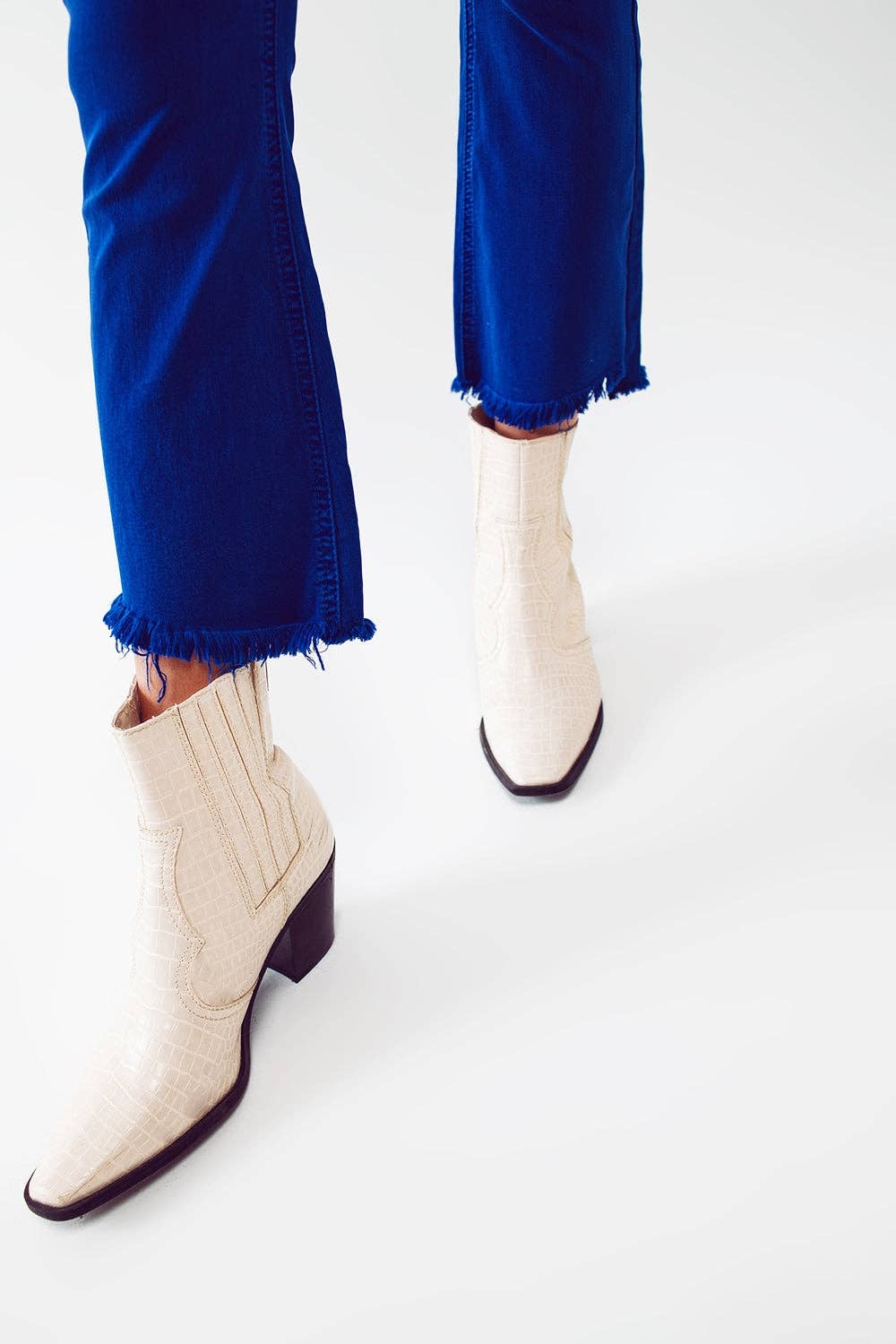 White ankle boots worn with royal  blue jeans  with frayed edge on a white background