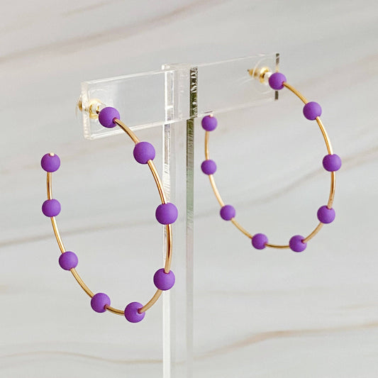 Purple beaded hoop earrings on a clear stand against a white background