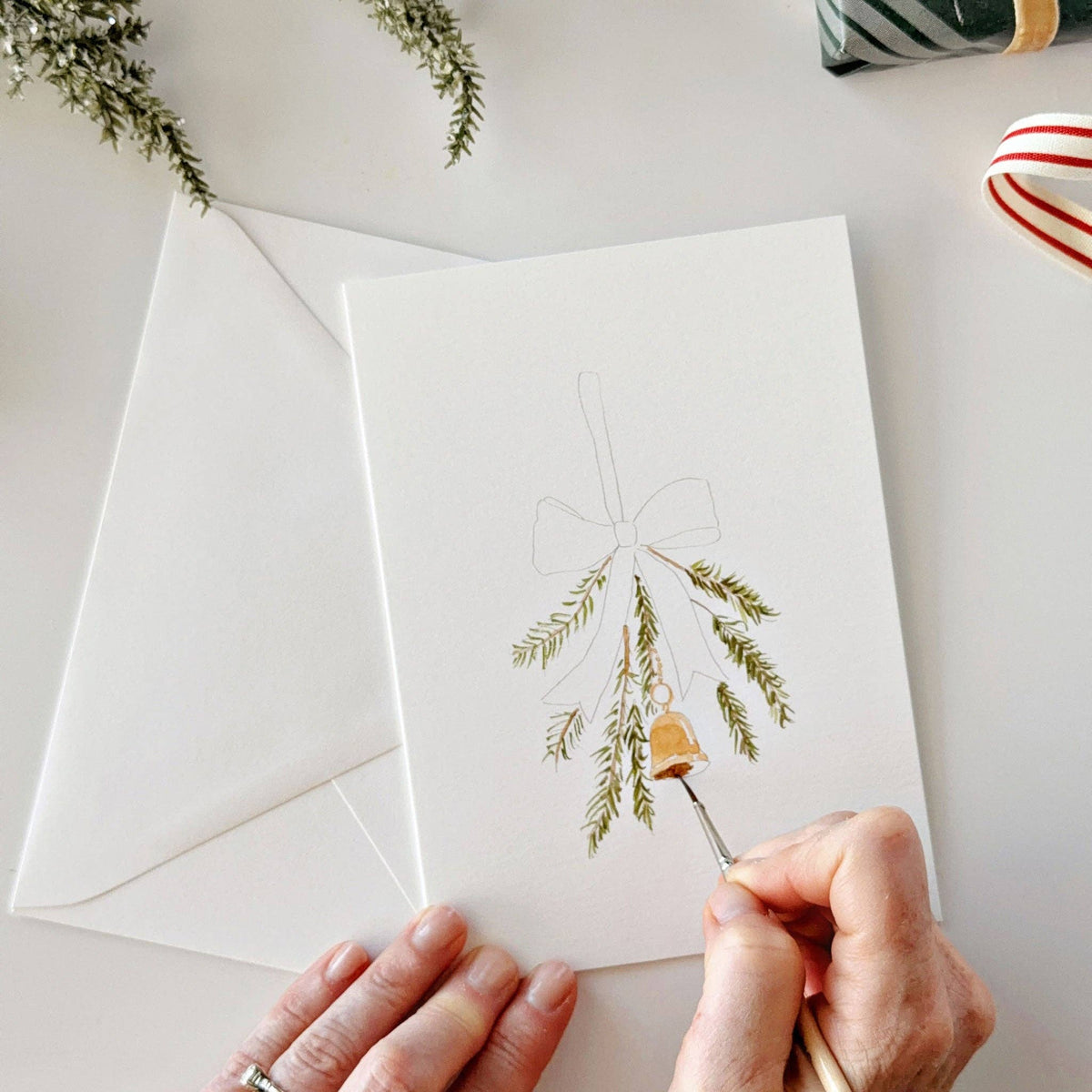 Painting greenery with a bell on a Christmas notecard