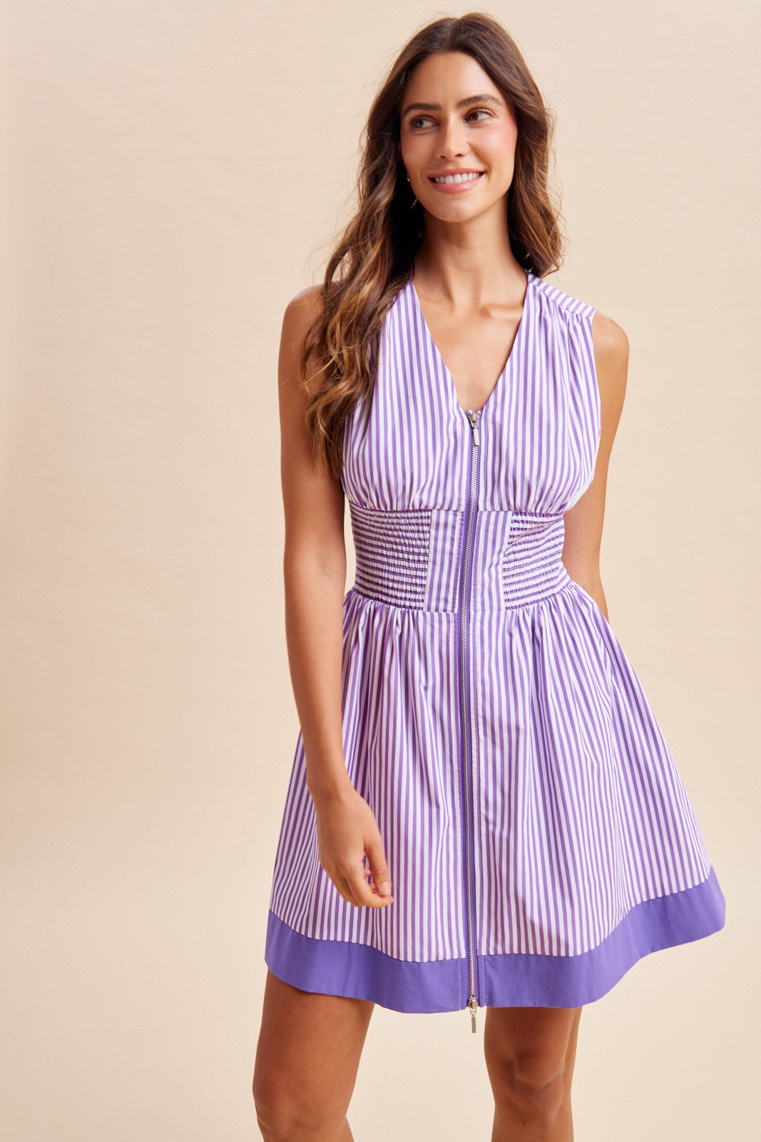 Woman wearing a purple and white striped dress against a beige background