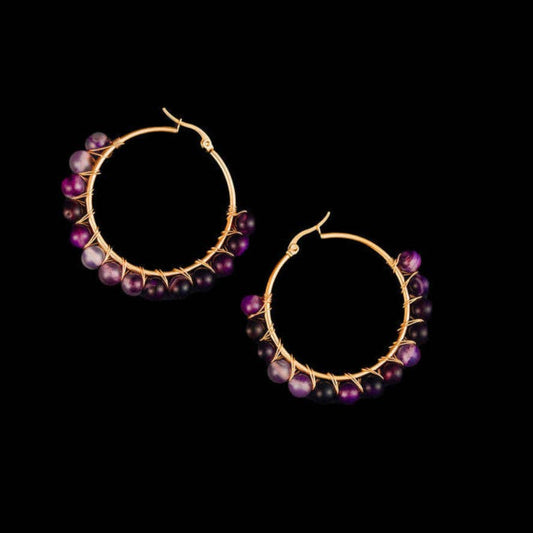 A pair of gold hoop earrings decorated with small purple and black beads, displayed against a solid black background.
