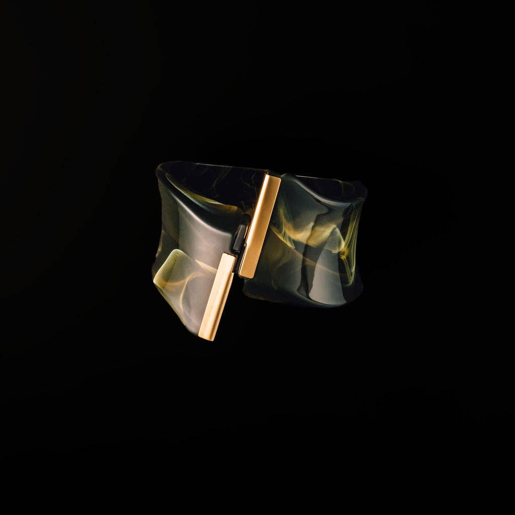 A wide, open cuff bracelet made of translucent smoky amber resin with gold-toned metal bars, shown against a solid black background.