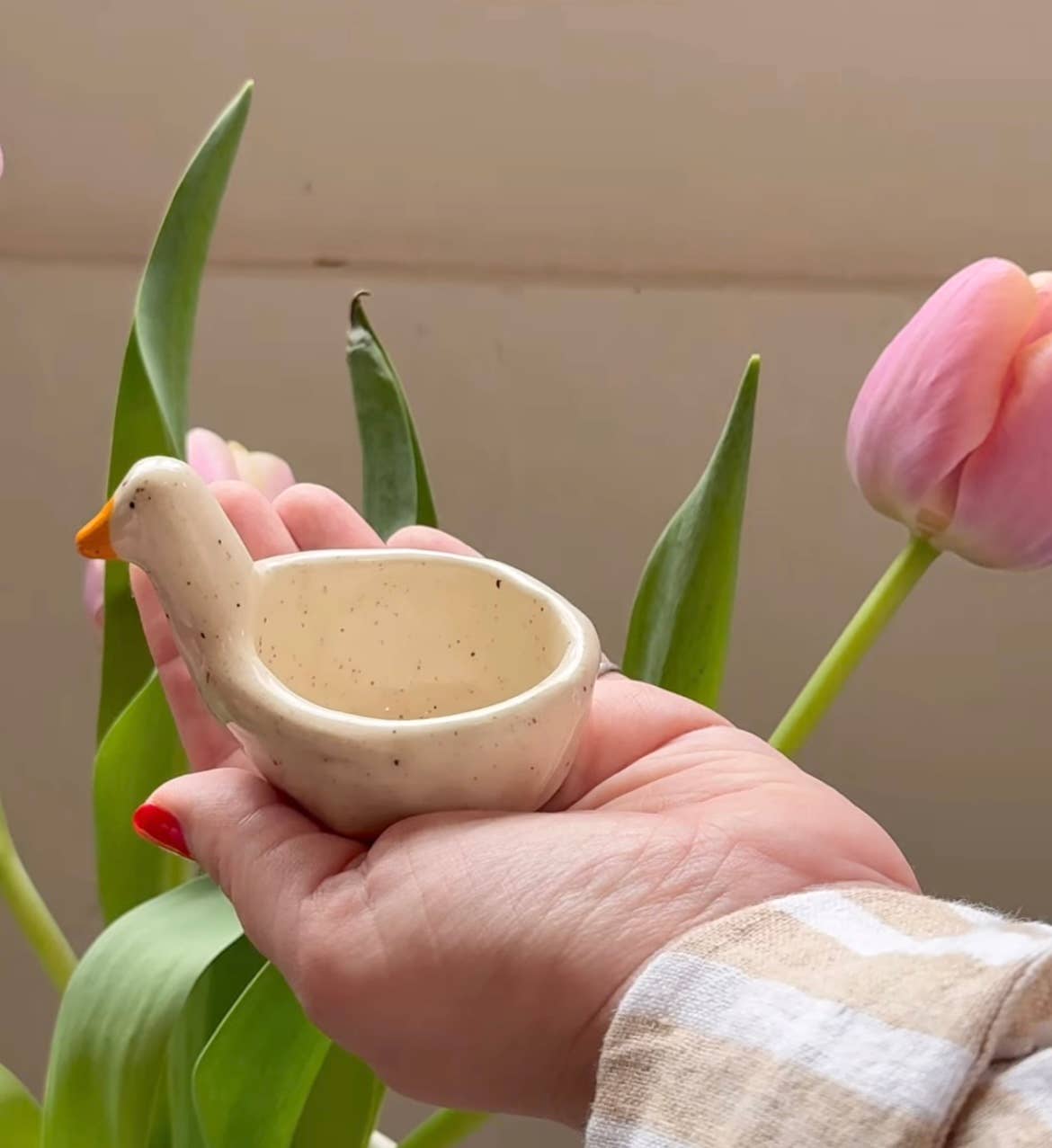 Hand holding the goose ring dish in front of pink tulips