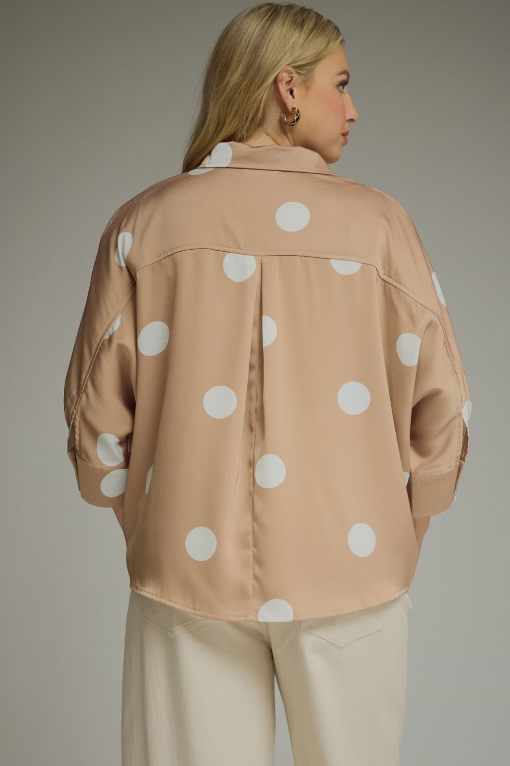 Woman wearing a beige jacket with white polka dots on a neutral background