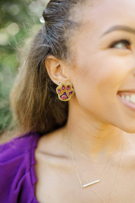 Close up of woman wearing purple and gold tiger paw studs outside 