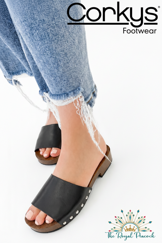A person wearing black slide sandals with distressed blue jeans, shown against a white background with promotional text for Corkys Footwear 
