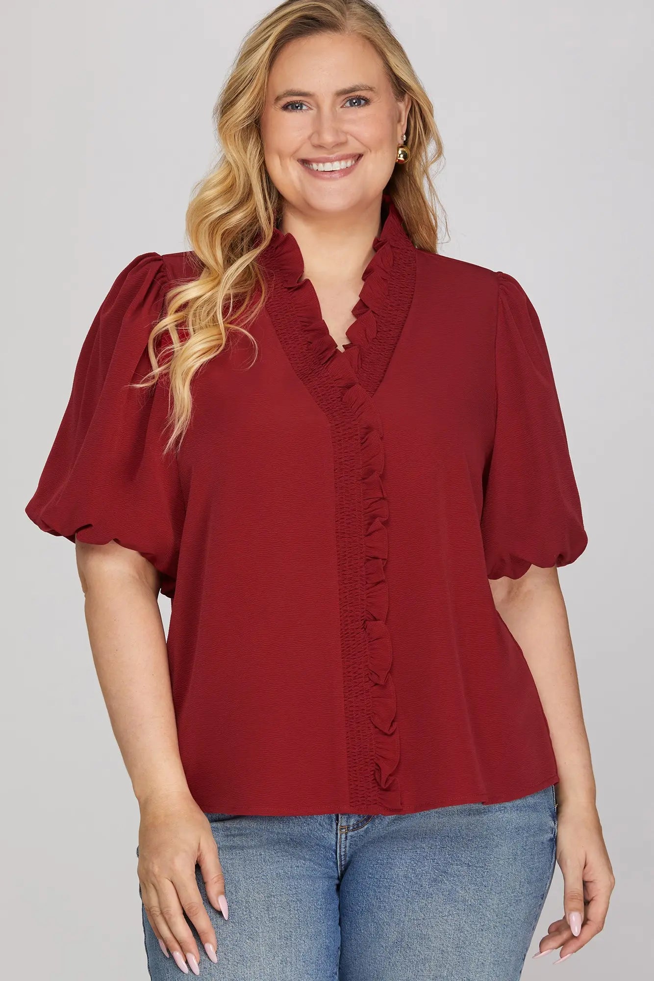 Woman wearing a wine blouse with short sleeves and blue jeans on a gray background