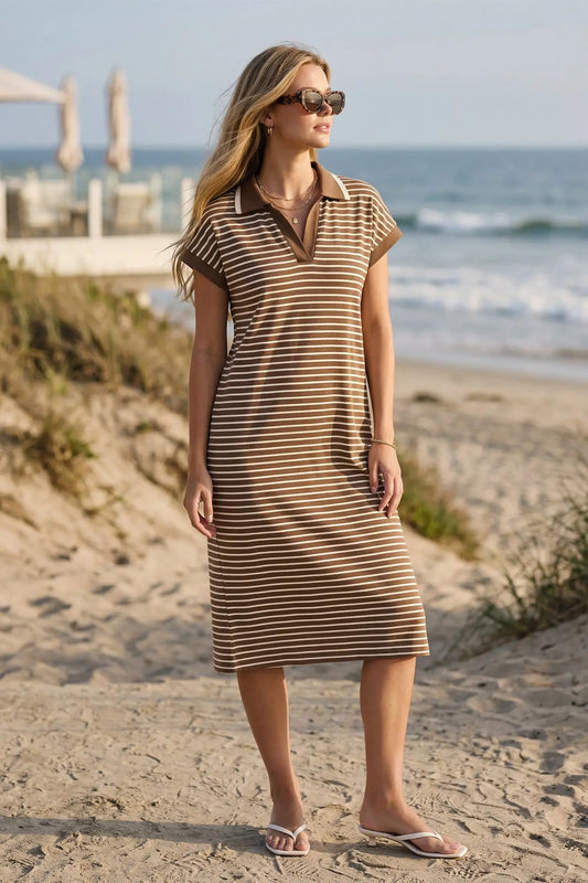 Woman in a mocha and off white striped dress standing on a sandy beach with ocean in the background
