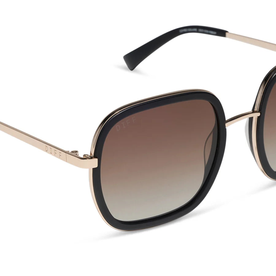 Close-up of a pair of sunglasses with a black acetate frame, gold metal rims and temples, and brown gradient lenses. The brand name 'DAPE' is visible on the temple and printed on the lens.