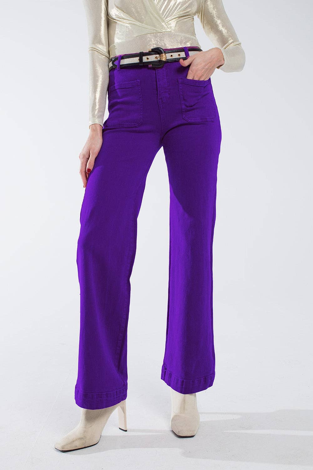 Person wearing purple jeans pants with front patch pockets and a gold top on a white background