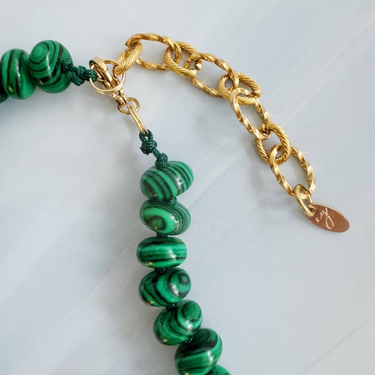 Green beaded bracelet with gold chain on a light gray background