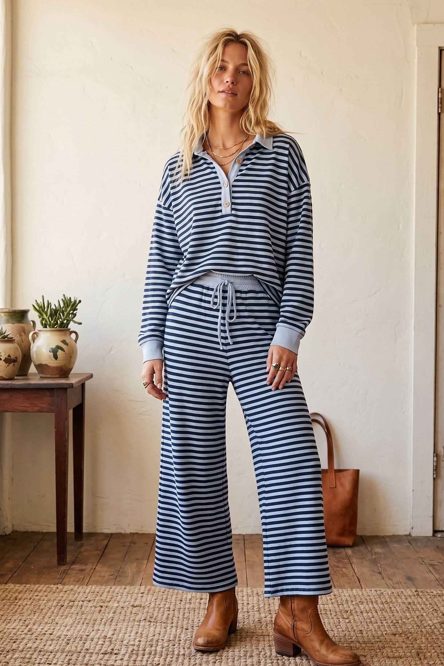 Woman wearing a blue and white striped outfit standing in a room with a wooden table and plants.