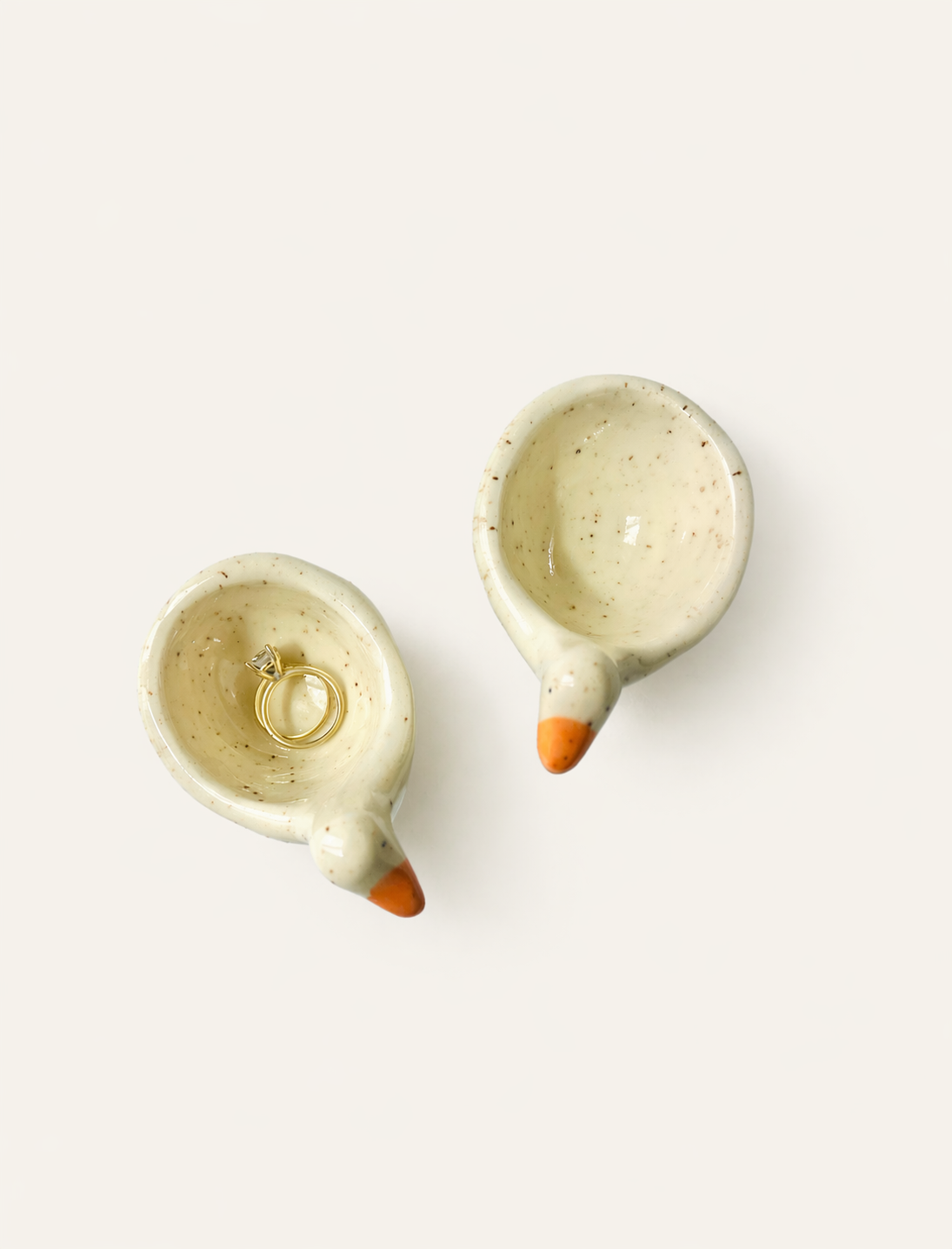 Two speckled goose ring dishes holding gold rings, viewed from above