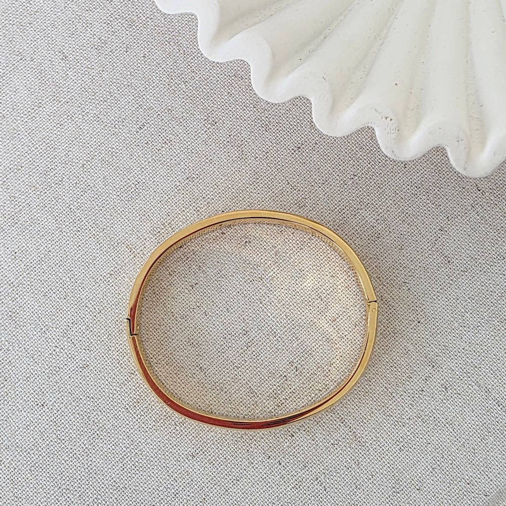 Gold bangle on a textured gray surface with a white shell in the background