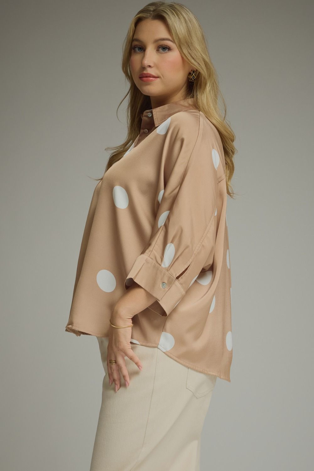 Woman wearing a beige blouse with white polka dots on a plain background
