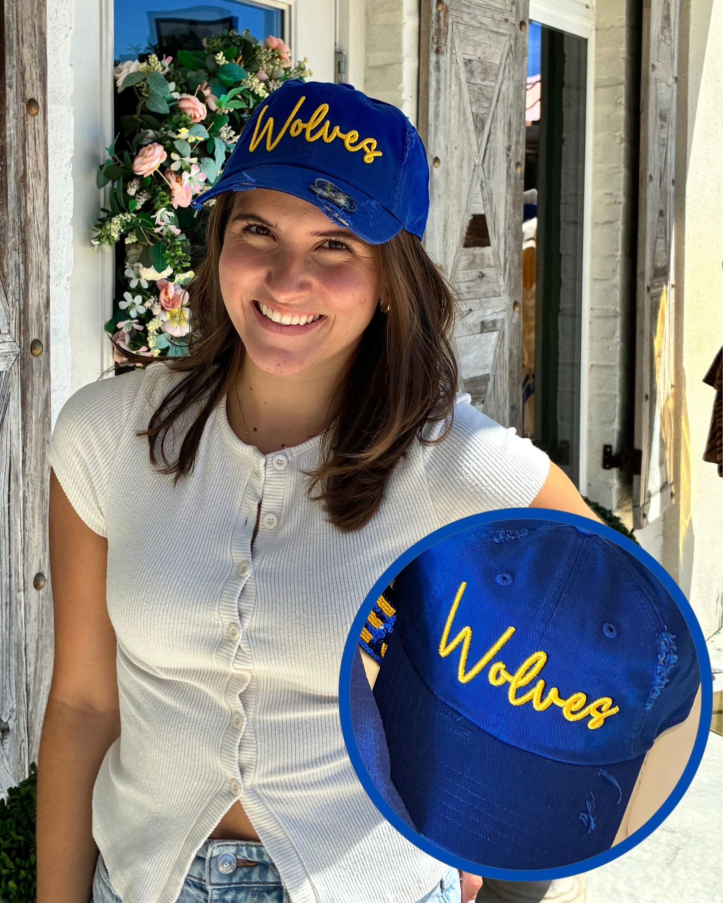 A woman wearing a royal blue baseball cap with yellow embroidered 'Wolves' text, shown outdoors in front of a rustic white wooden building. A circular inset provides a close-up of the cap's front panel and embroidery.