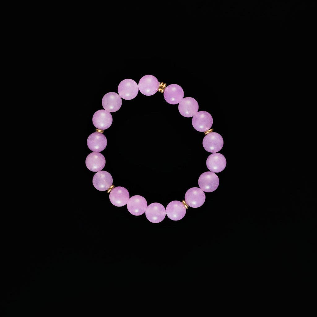 A beaded stretch bracelet made of smooth, light purple lavender beads separated by small gold spacer rings, displayed on a solid black background.
