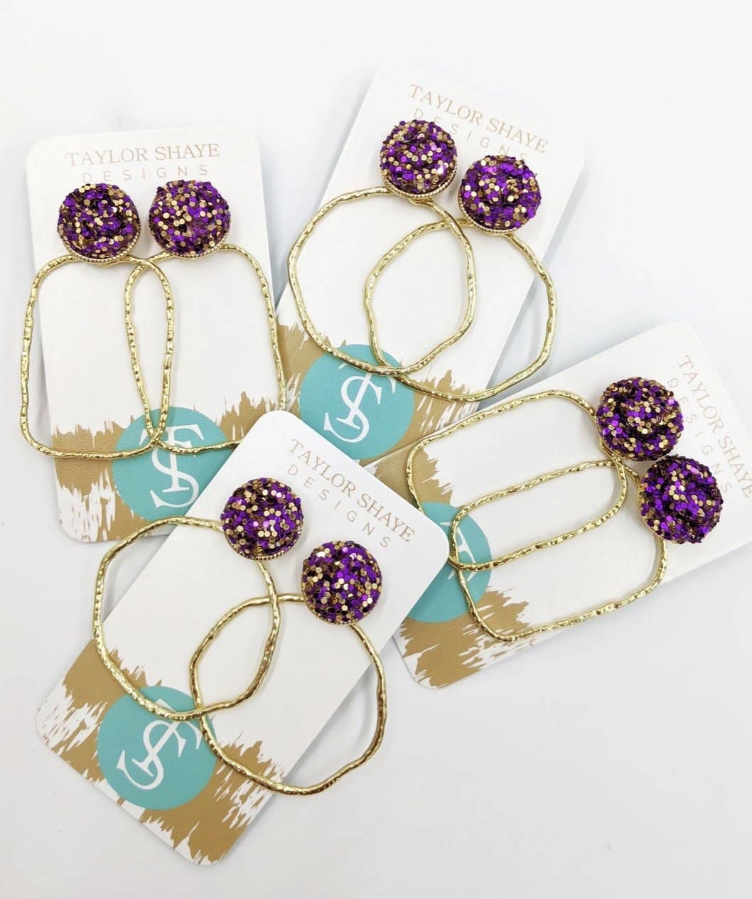 Purple and gold earrings on Taylor Shaye branded cards.