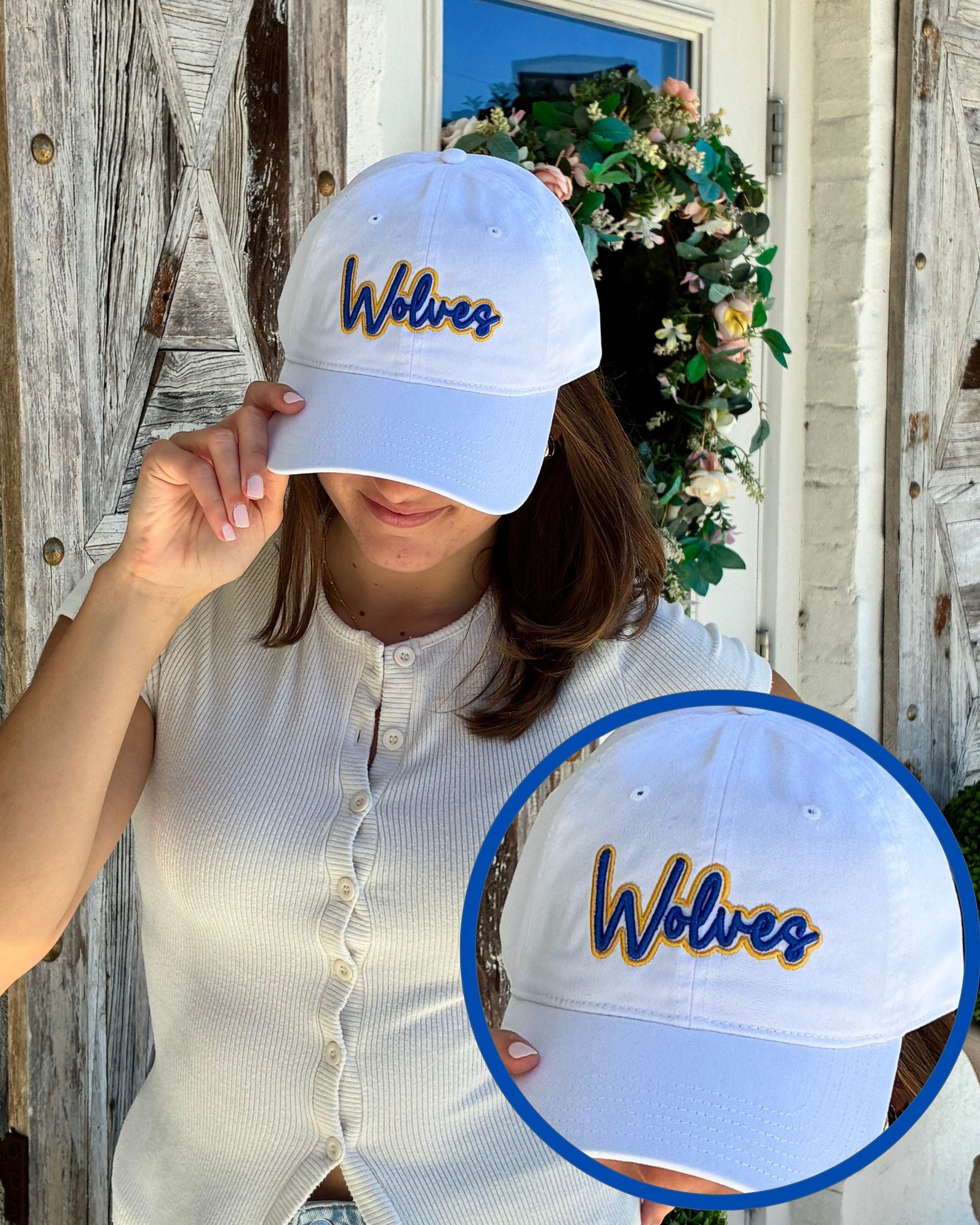 A woman wearing a white baseball cap with 'Wolves' embroidered in blue and gold on the front, standing outdoors in front of a rustic wooden door and floral wreath. A circular inset shows a close-up of the cap's front embroidery.