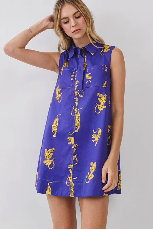 A woman wearing a sleeveless purple shirt dress with a yellow tiger print, photographed against a light gray studio background.