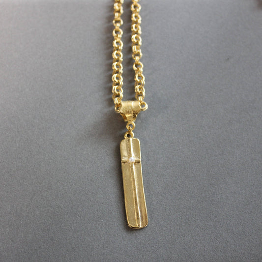 A gold necklace with a polished rectangular bar pendant featuring a raised cross detail, displayed on a neutral gray background.