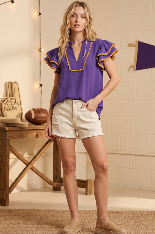 Woman wearing a purple blouse with ruffled details and white shorts in a casual setting.