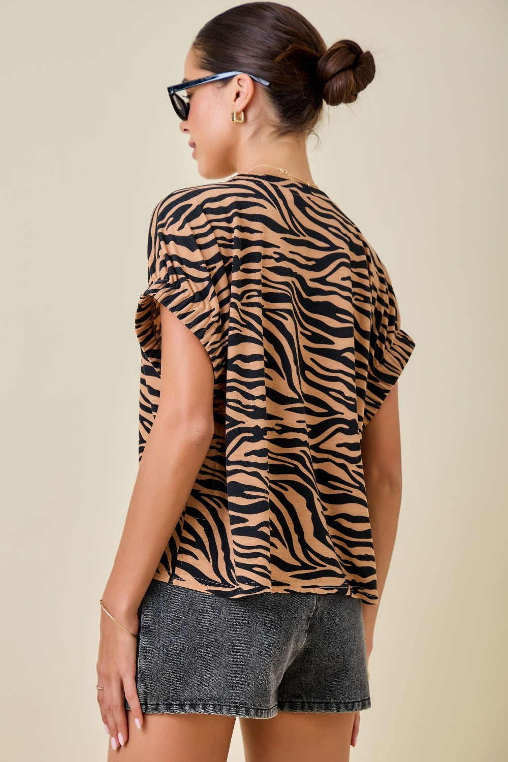 Woman wearing a tiger print top and denim shorts on a beige background