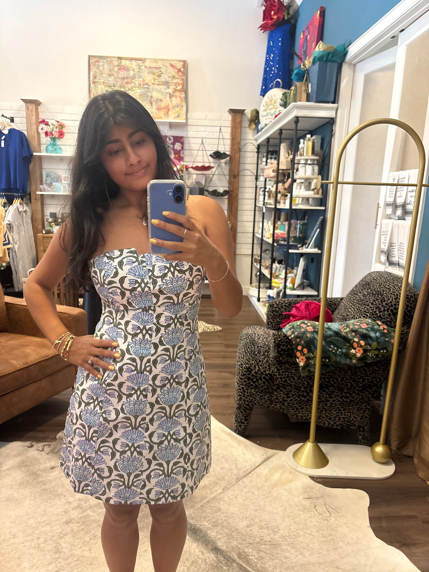 A woman taking a mirror selfie in a boutique, wearing a strapless sleeveless dress with a blue, gray, and white geometric pattern.