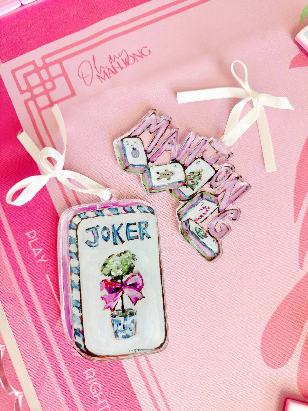 Mahjong Joker and Mahjong Christmas acrylic ornaments with white ribbons on a pink Mahjong mat