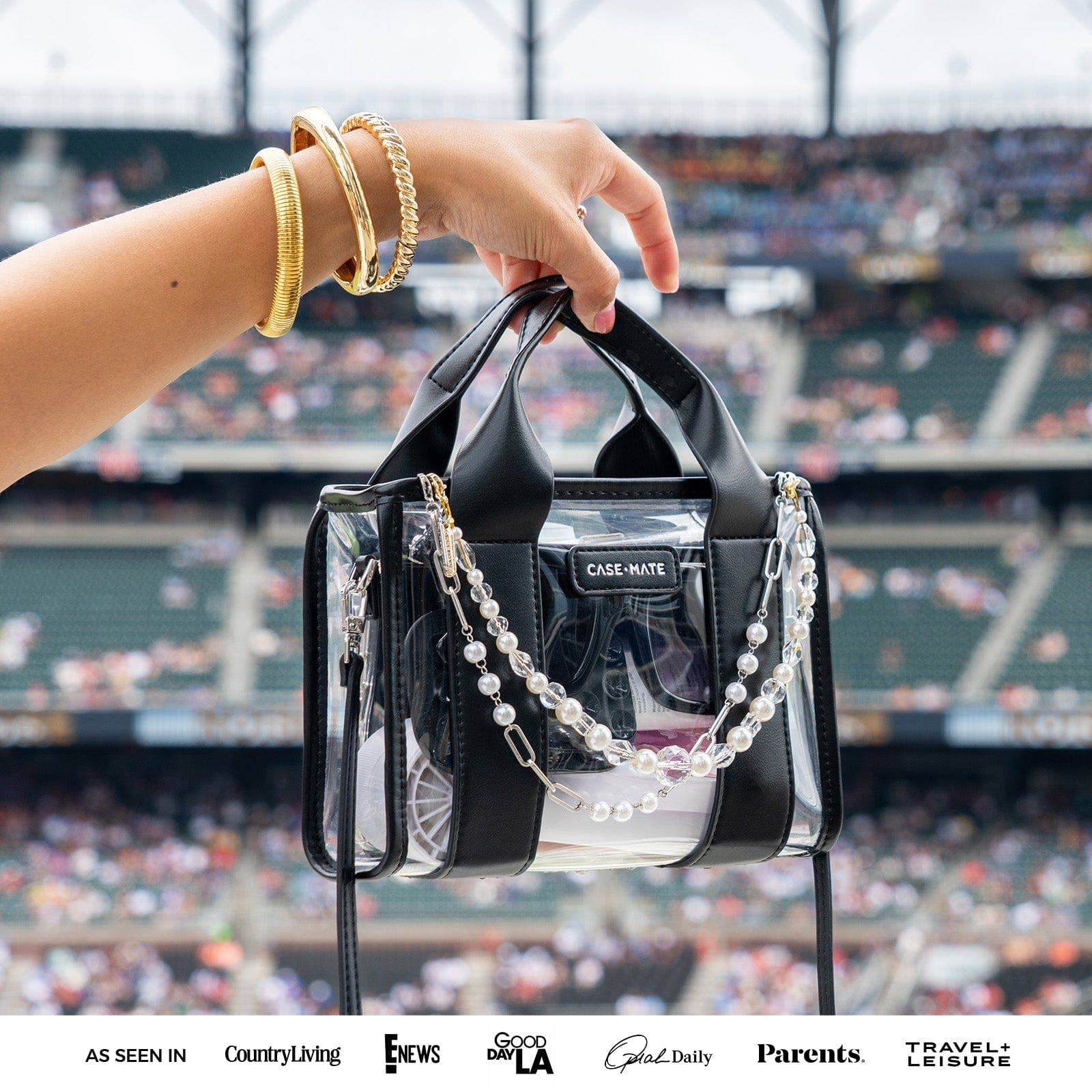 Person holding a clear handbag with black accents at a sports event.