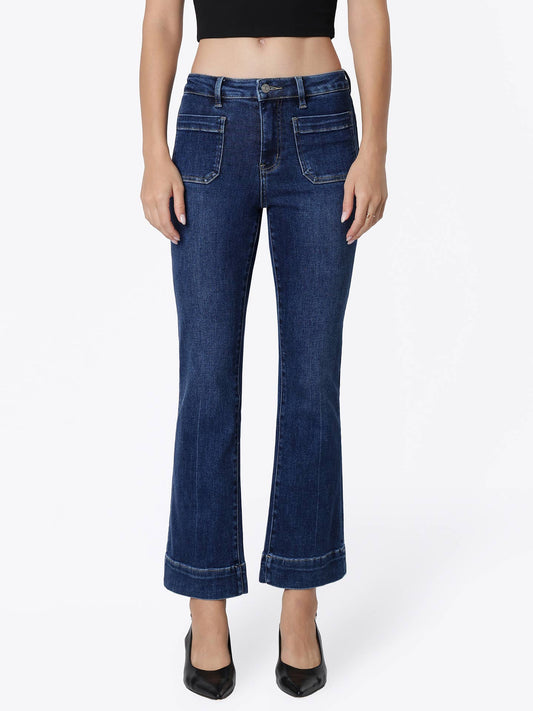 A model wearing a pair of dark blue flare jeans with finished  hems and black heels, shown from the waist down against a plain white studio background.