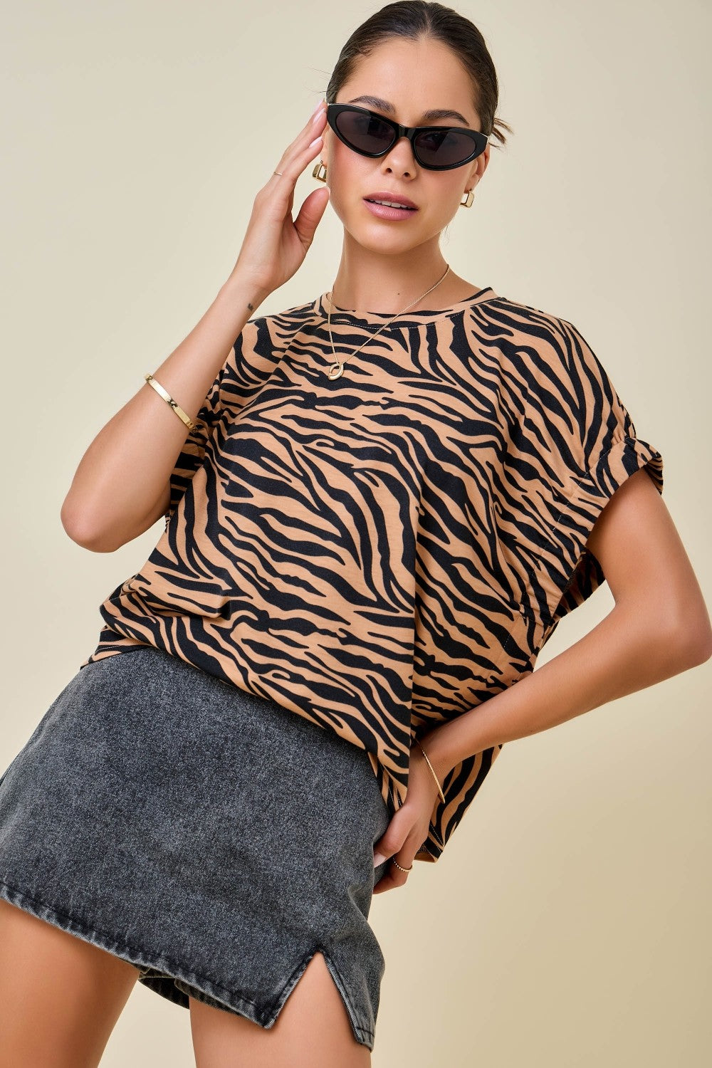 Woman wearing a tiger or zebra  print top and denim skirt on a beige background