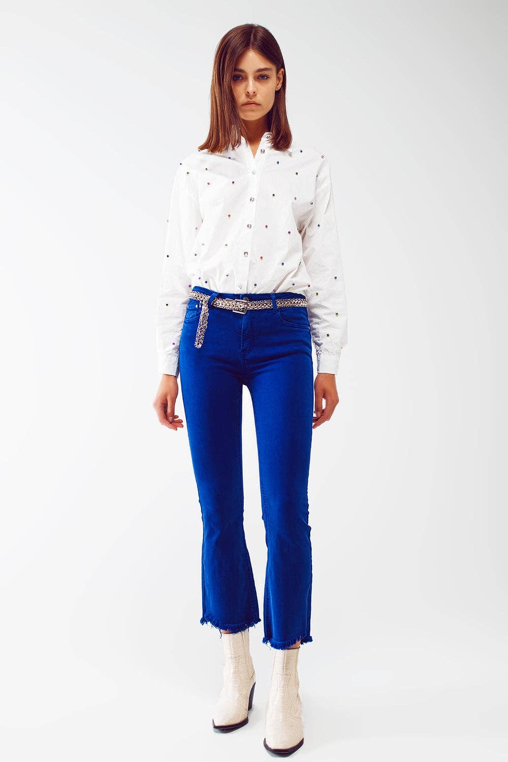 Woman wearing a white blouse with black polka dots and blue jeans on a white background