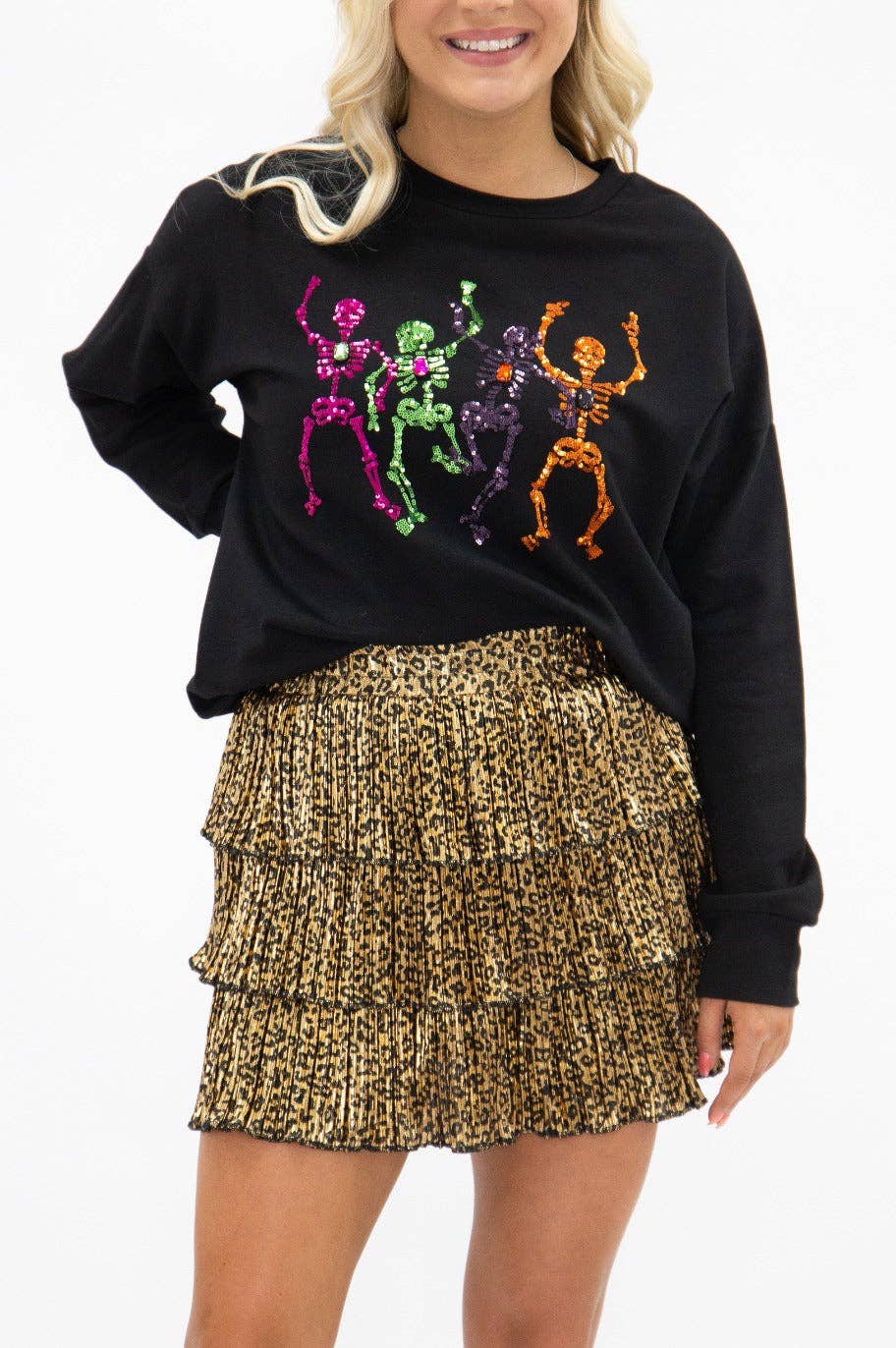 Person wearing a black sweatshirt with colorful skeleton designs and a gold patterned skirt.