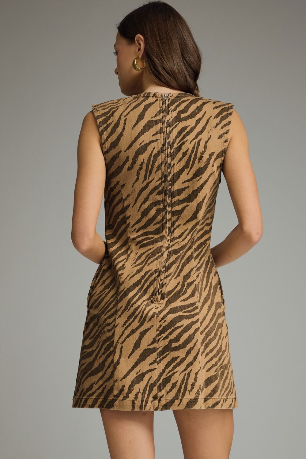 A woman shown from the back wearing a sleeveless mini dress with a brown and tan zebra-like animal print pattern, photographed against a plain gray studio background.