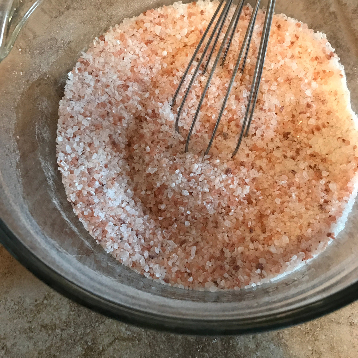 Pink and white bath salts being mixed in a glass bowl