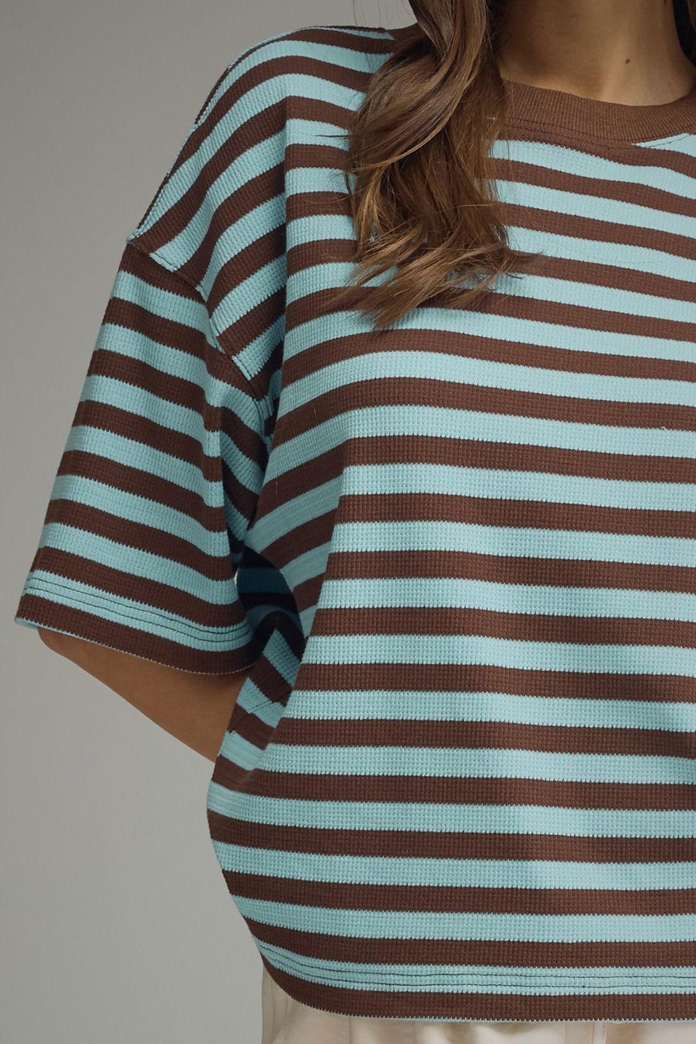 A close-up of a person wearing an oversized short-sleeve knit top with horizontal brown and light aqua stripes.