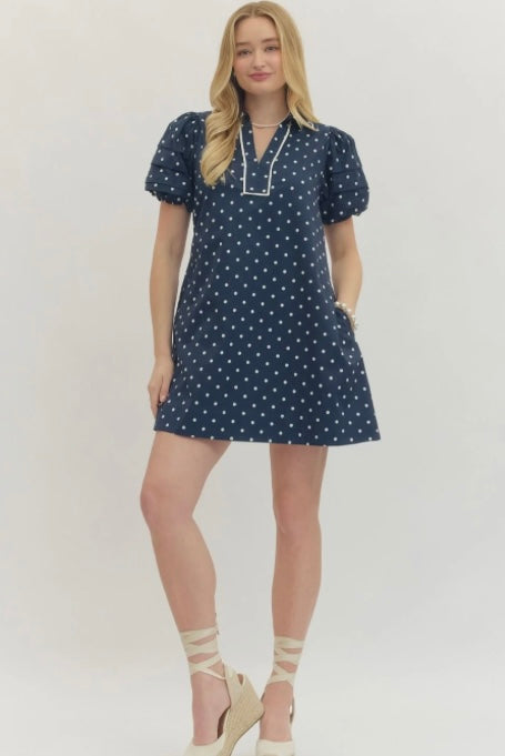 Woman wearing a navy blue dress with white polka dots on a plain background