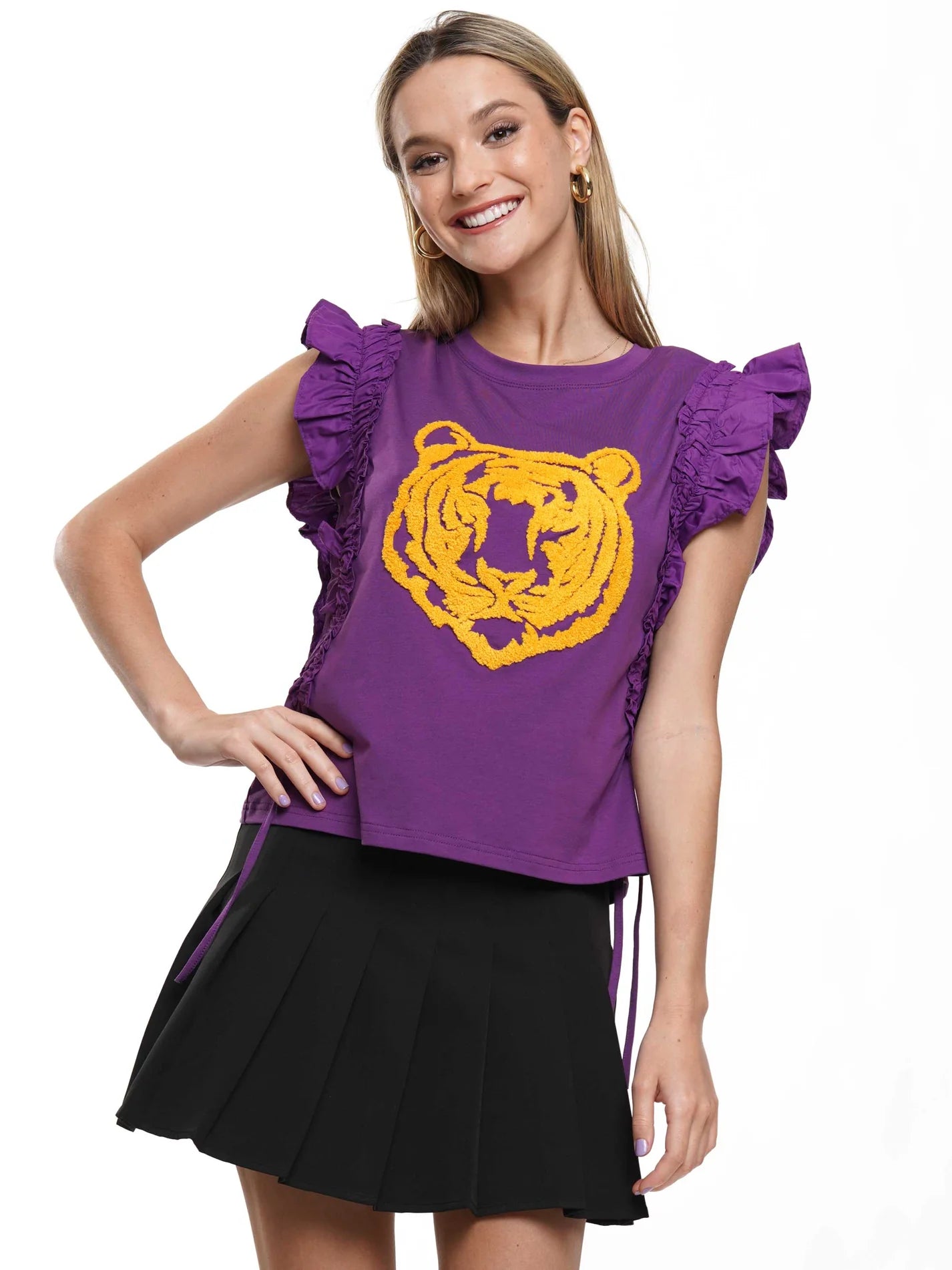 A woman modeling a purple short-sleeve top with ruffled shoulders and a large yellow tiger graphic on the front, paired with a black pleated skirt, against a plain white background.